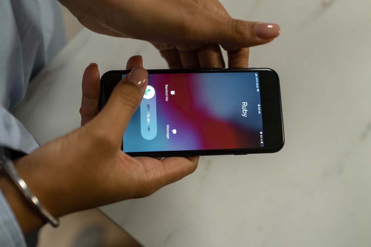 Hands holding a smartphone showing an incoming phone call, representing AI voice cloning scam calls