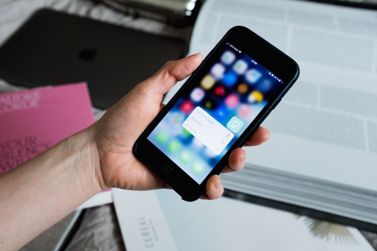 Hand holding a smartphone showing a home screen with app icons and a delete-app popup, representing fake clone apps