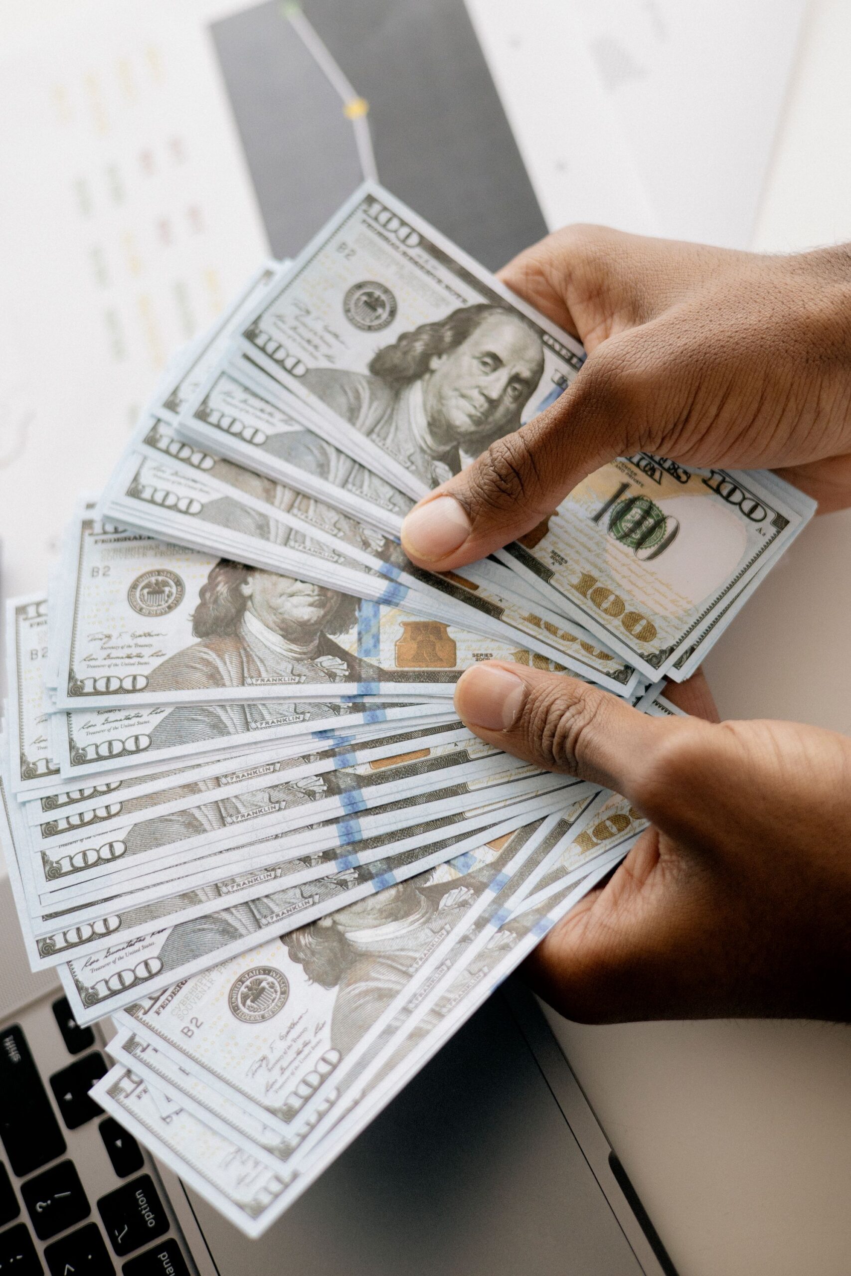 Illustrative close-up of hands counting cash near a laptop, representing an upfront fee paid to start a data entry job