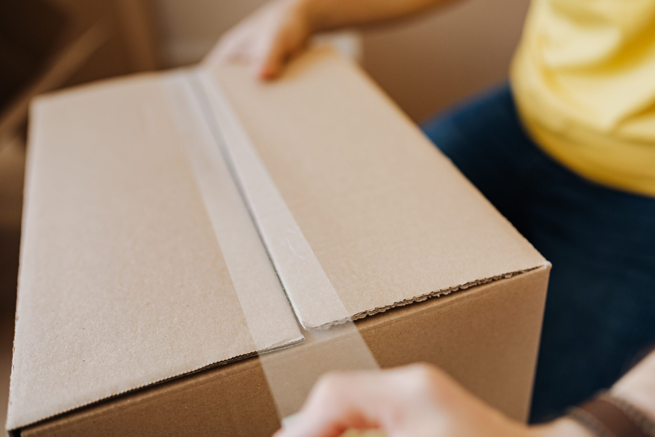 Illustrative photo of someone sealing a cardboard box, representing a reshipping or package-forwarding job scam
