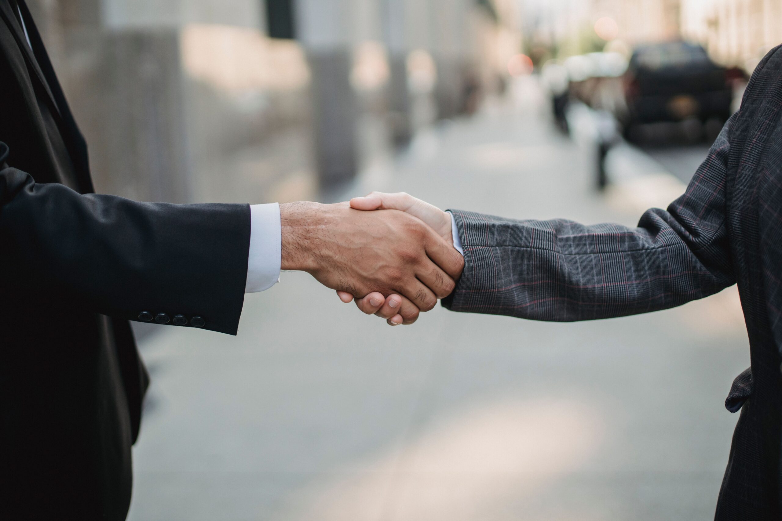 Close-up of two people in business attire shaking hands outdoors, symbolizing a partnership or investment agreement