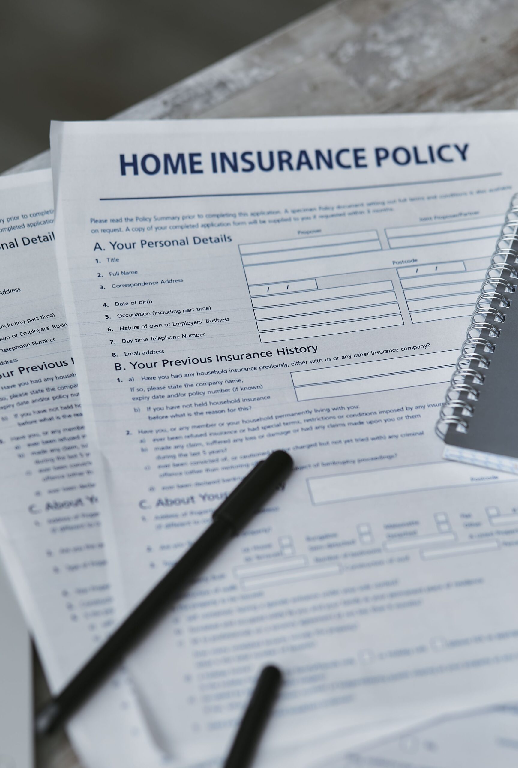 Flatlay of a home insurance policy form and notebook on a table with a pen, representing an insurance policy document