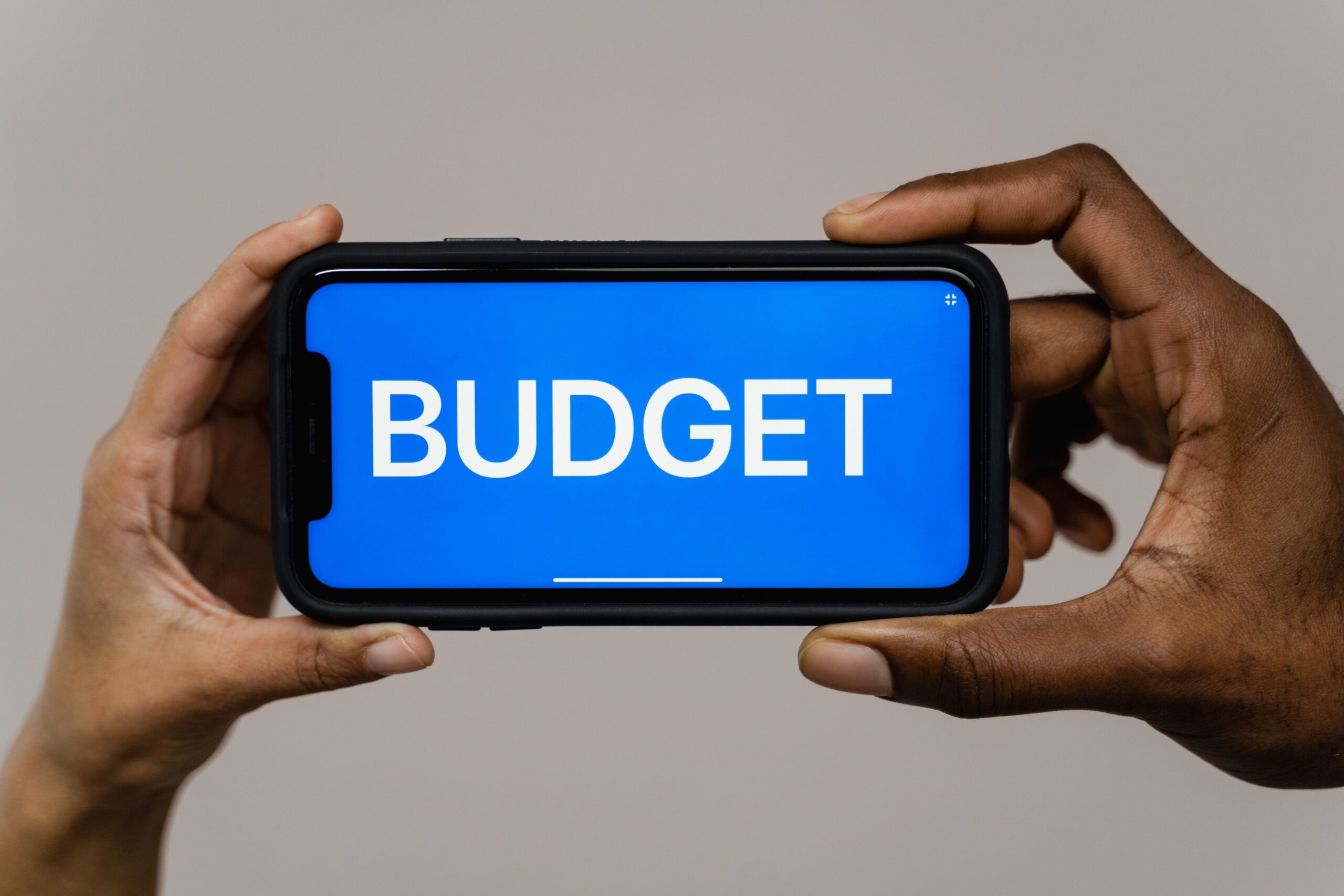 Two hands holding a smartphone displaying the word Budget on the screen, representing a finance or loan app