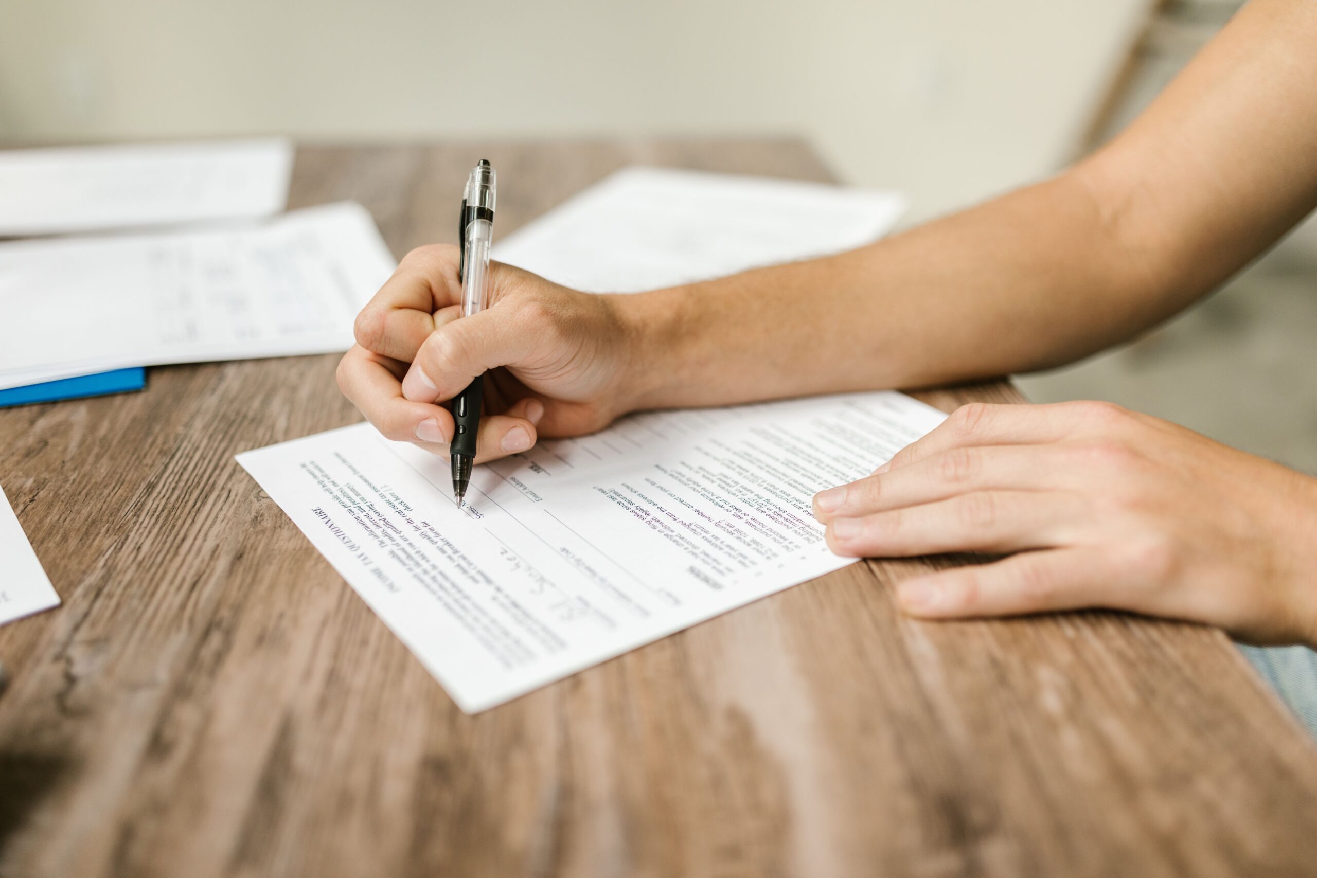 Close-up of a hand filling out a paper form with a pen, representing a government scheme or subsidy application