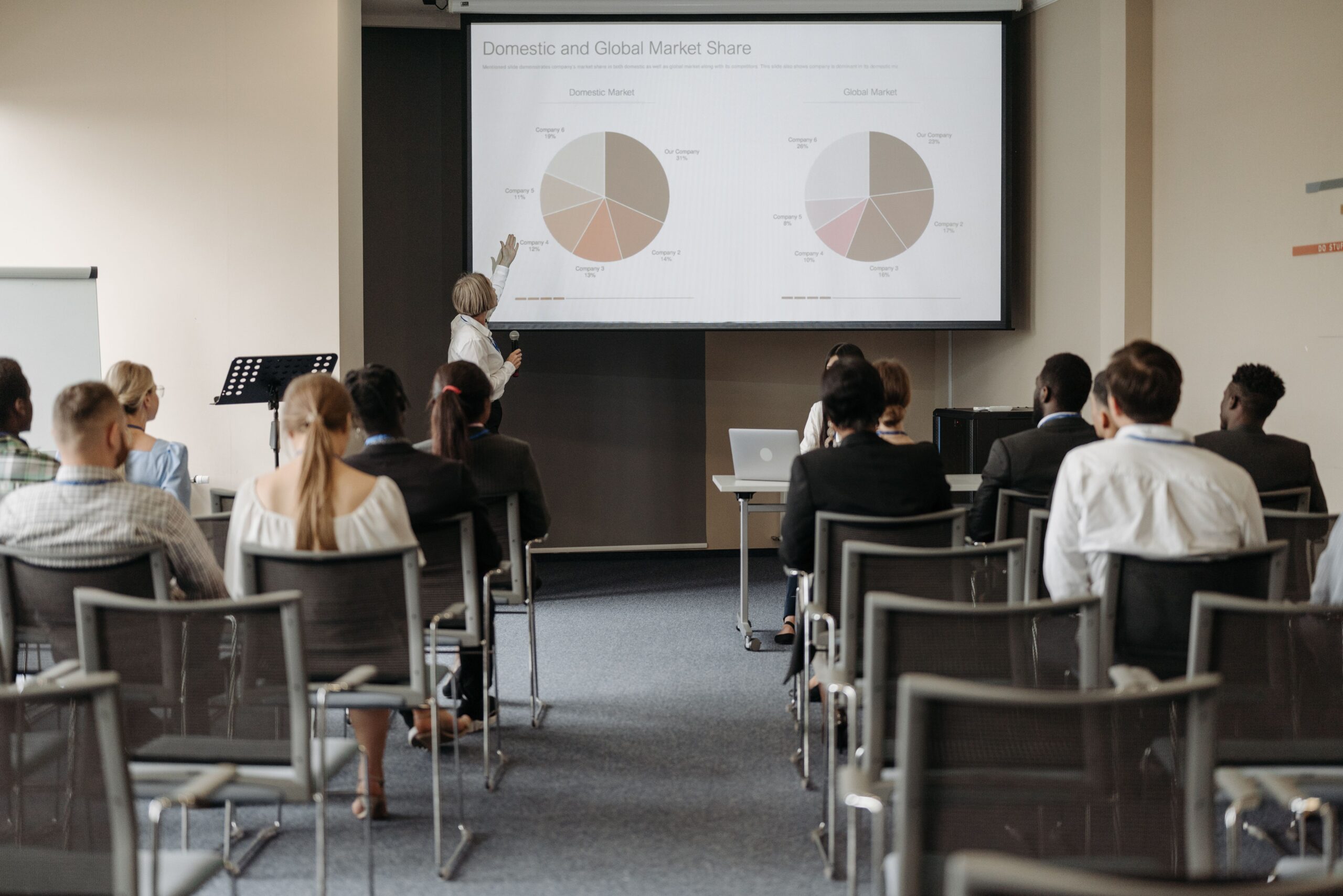Rear view of an audience watching a presenter and market share charts at a business conference