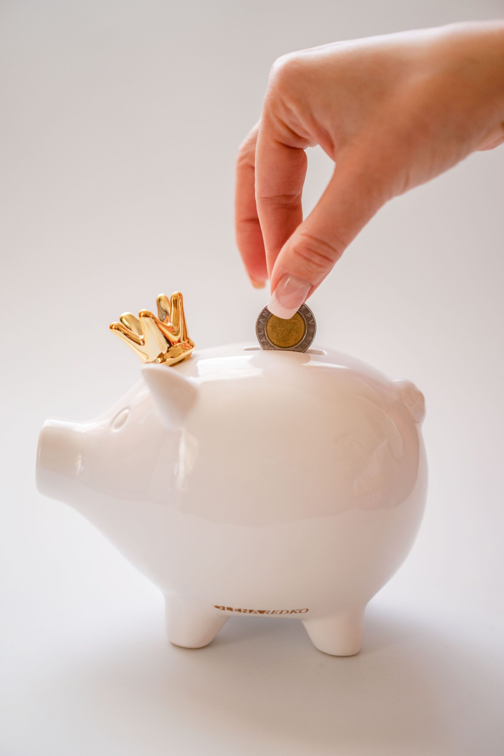 Close-up of a hand depositing a coin into a white piggy bank, representing a donation or crowdfunding contribution