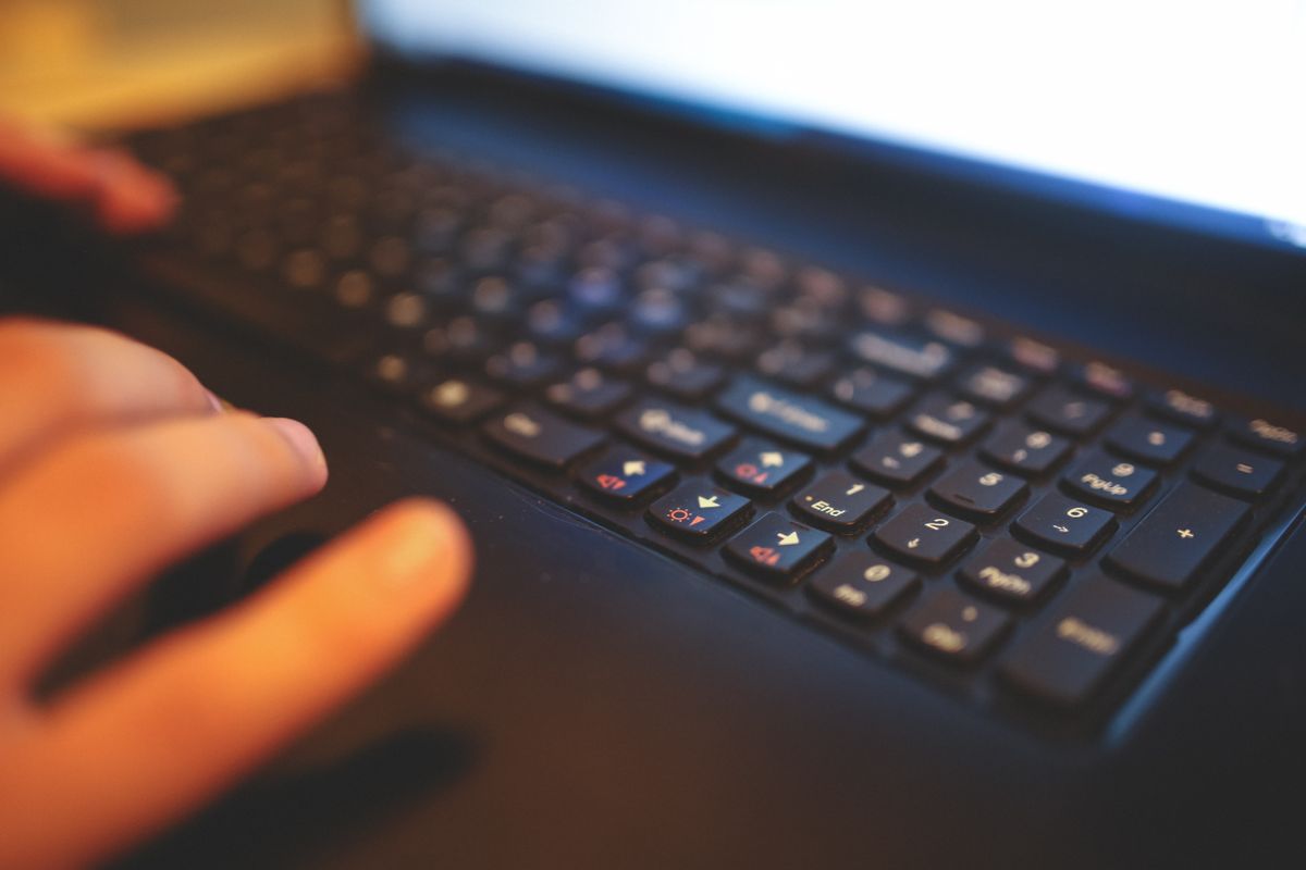 Close-up of hands typing on a laptop keyboard with a blurred bright screen, representing phishing email scams
