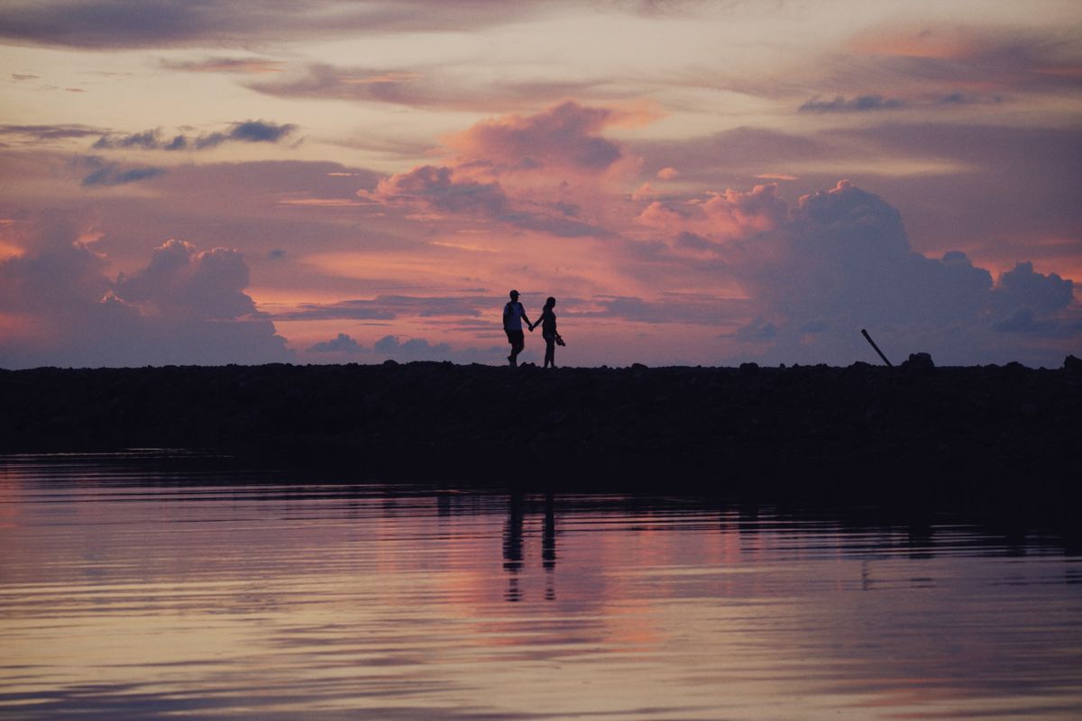 Silhouette of a couple holding hands by a lake at sunset, representing online romance scams