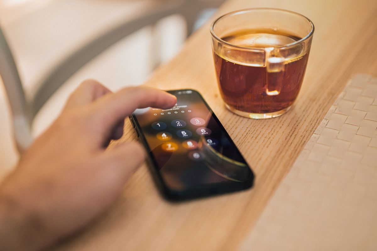 Hand entering a passcode on a smartphone next to a cup of tea, representing SIM swap account security